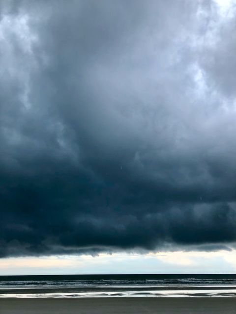 A dark shelf cloud rolling in over a pale beach