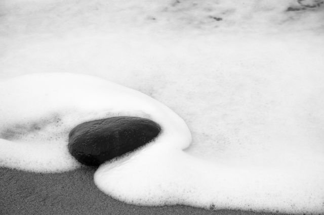 A dark stone wrapped in a curve of white sea foam, black and white
