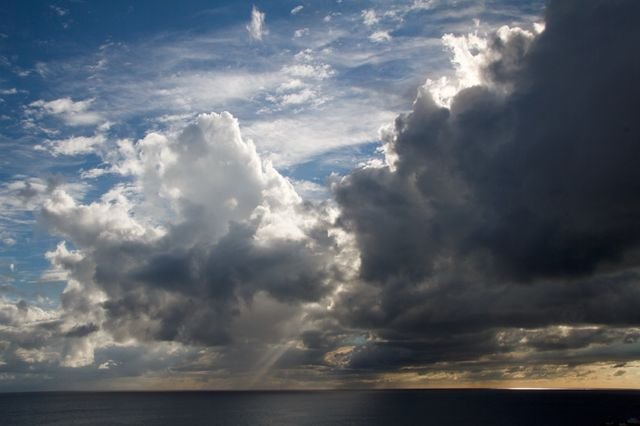 Storm towers over the open ocean, rain shafts and sunbeams trading places on the horizon