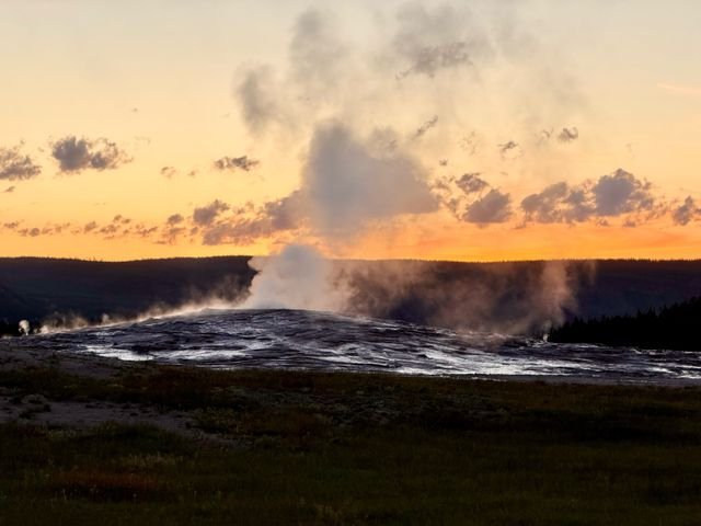 Old Faithful steaming against an orange dusk sky