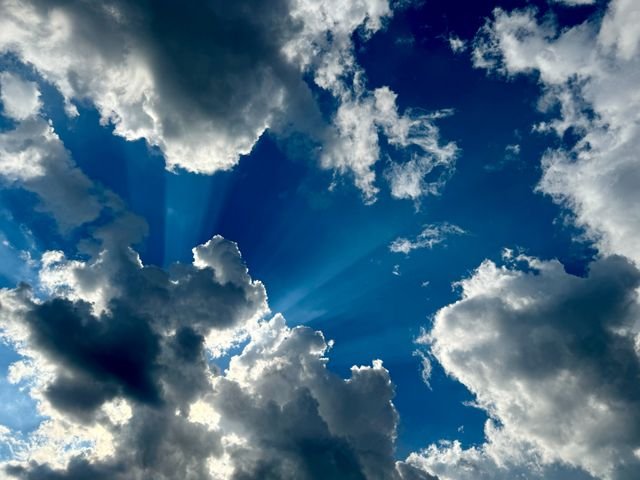 Sunbeams breaking around backlit cumulus in a deep blue sky